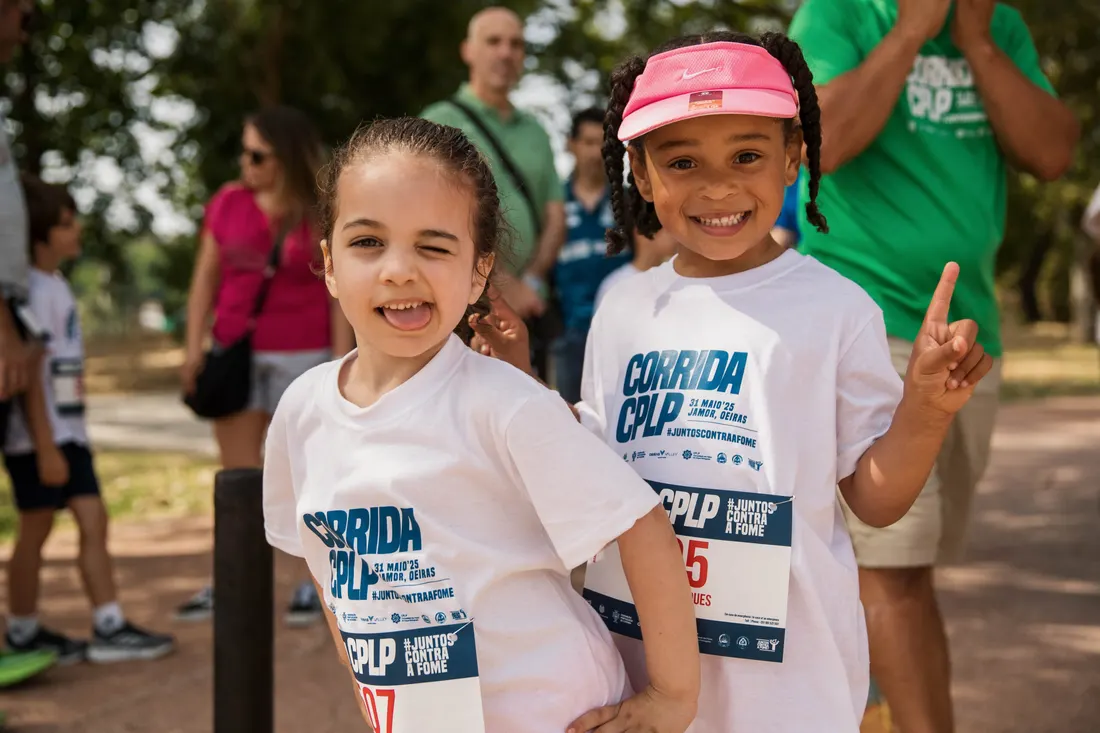 Duas crianças com camisolas da Corrida CPLP sorriem para a fotografia.